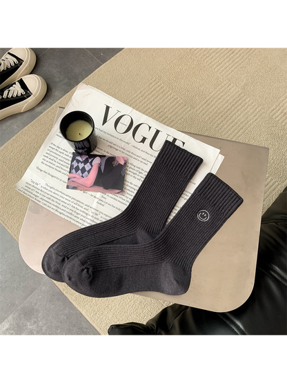 Dark gray ribbed crew socks with embroidered smiley motif, pair laid flat