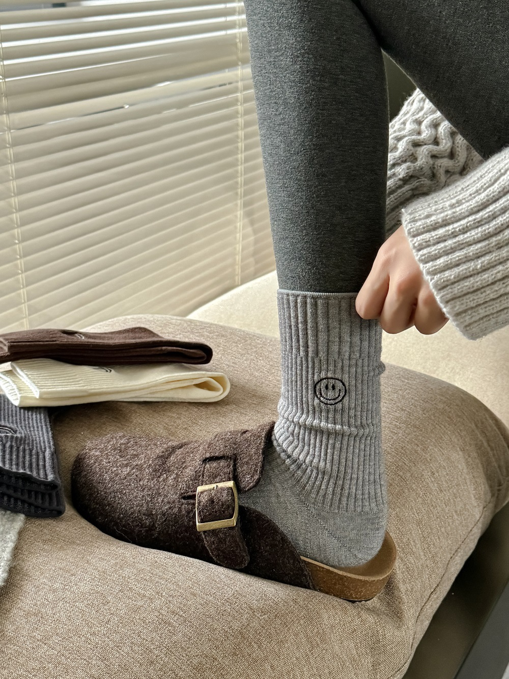 Light gray ribbed smiley crew sock worn with dark leggings and a brown clog
