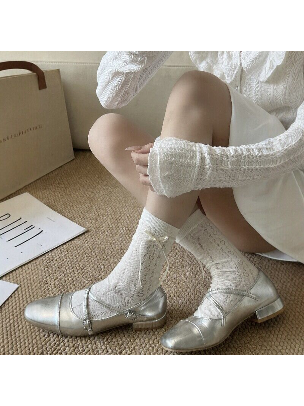 Ivory patterned crew socks styled with silver strap shoes in a seated view
