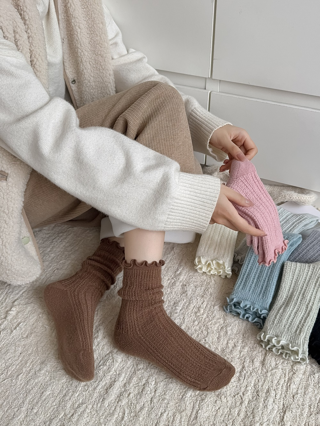 Brown ruffle-cuff socks worn while a pink pair is held beside other colors