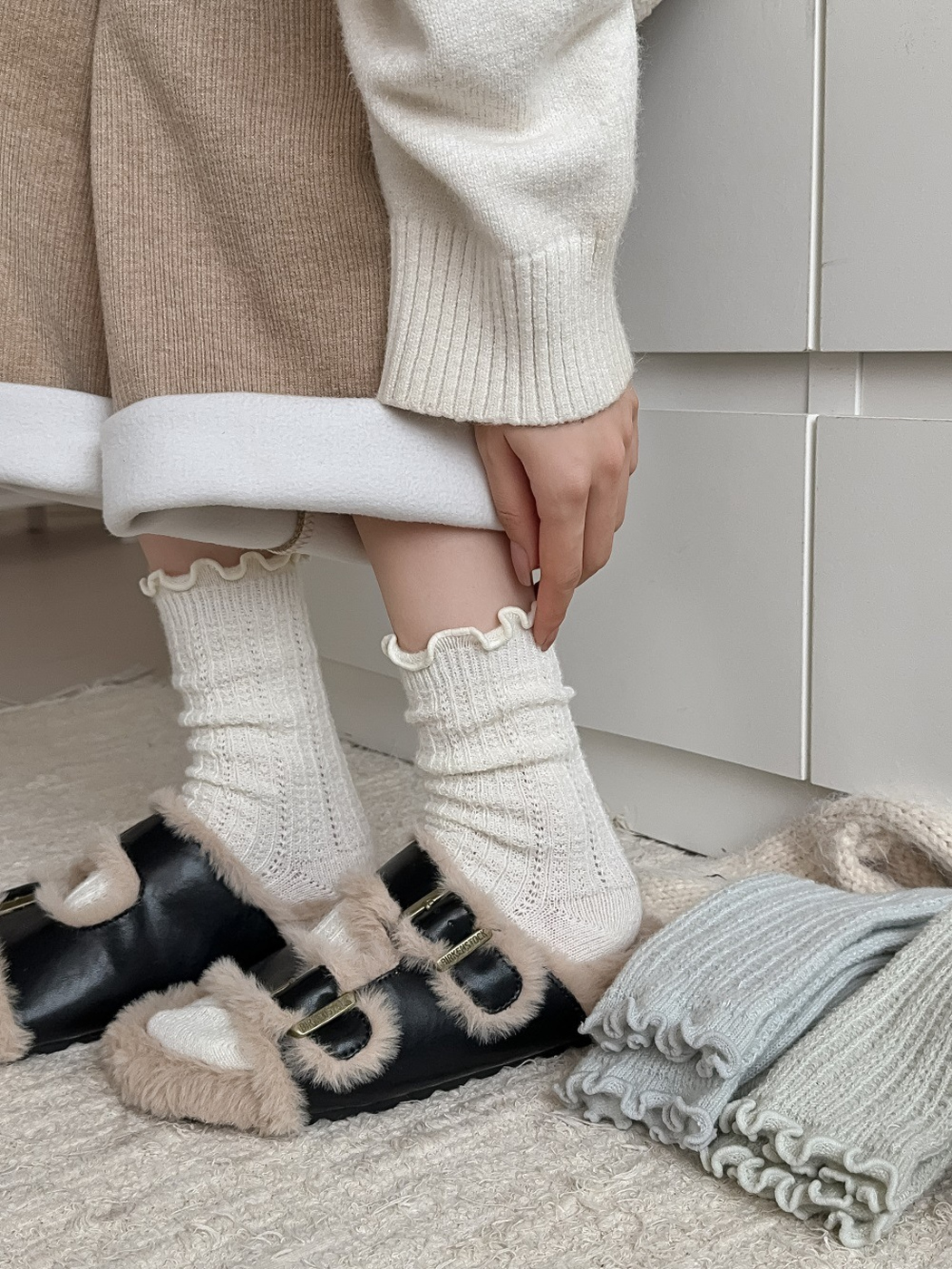 Ivory ruffle-cuff socks worn with plush buckle slippers