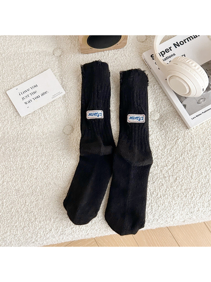 Black ribbed crew socks with distressed openings and sewn label patches