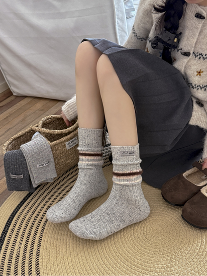 Light gray crew socks with fuzzy brown bands worn in a seated indoor setting