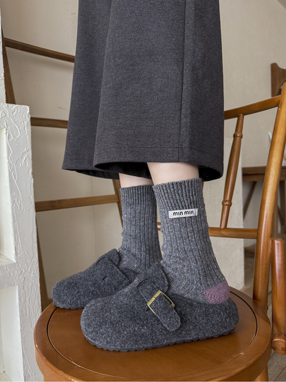Dark gray speckled crew socks with purple heels worn with gray felt clogs