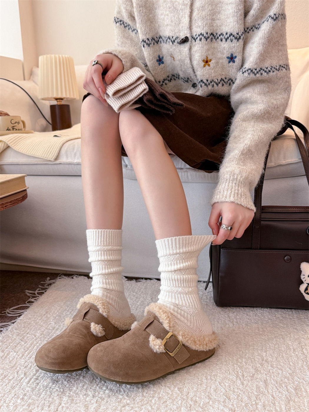 Ivory crew socks worn with clogs and folded neutral colors held above