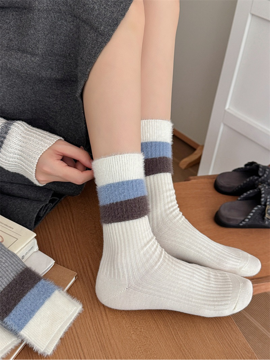 Cream ribbed crew socks with fuzzy blue and brown striped cuffs, worn without shoes