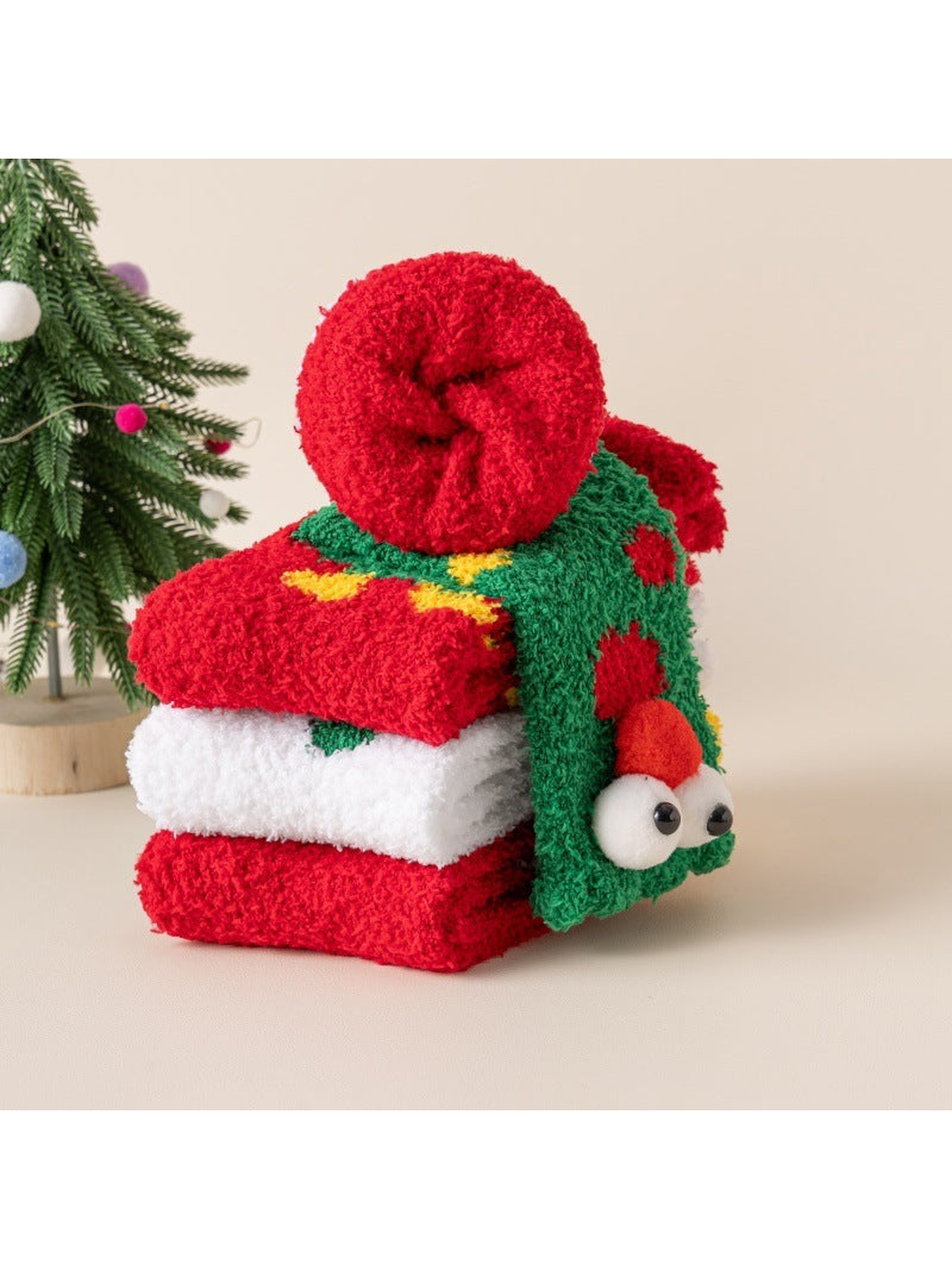 Fuzzy Christmas socks folded, stacked and rolled beside a decorated tree