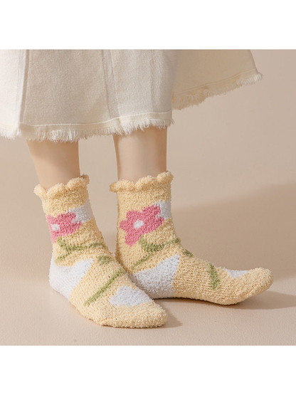 Yellow fuzzy crew socks with pink flowers worn against a neutral background