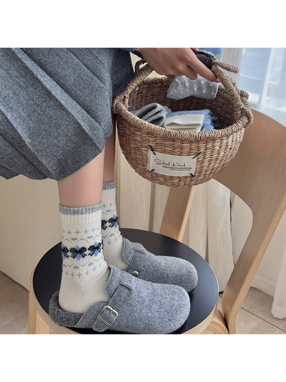 Cream bow-pattern crew socks worn with gray clogs beside a woven basket