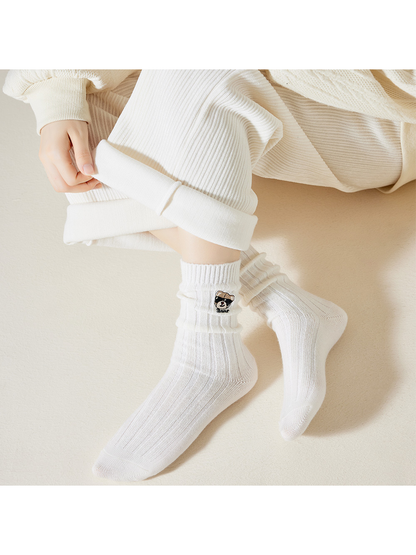 White ribbed bear-embroidered crew socks worn in a relaxed seated pose