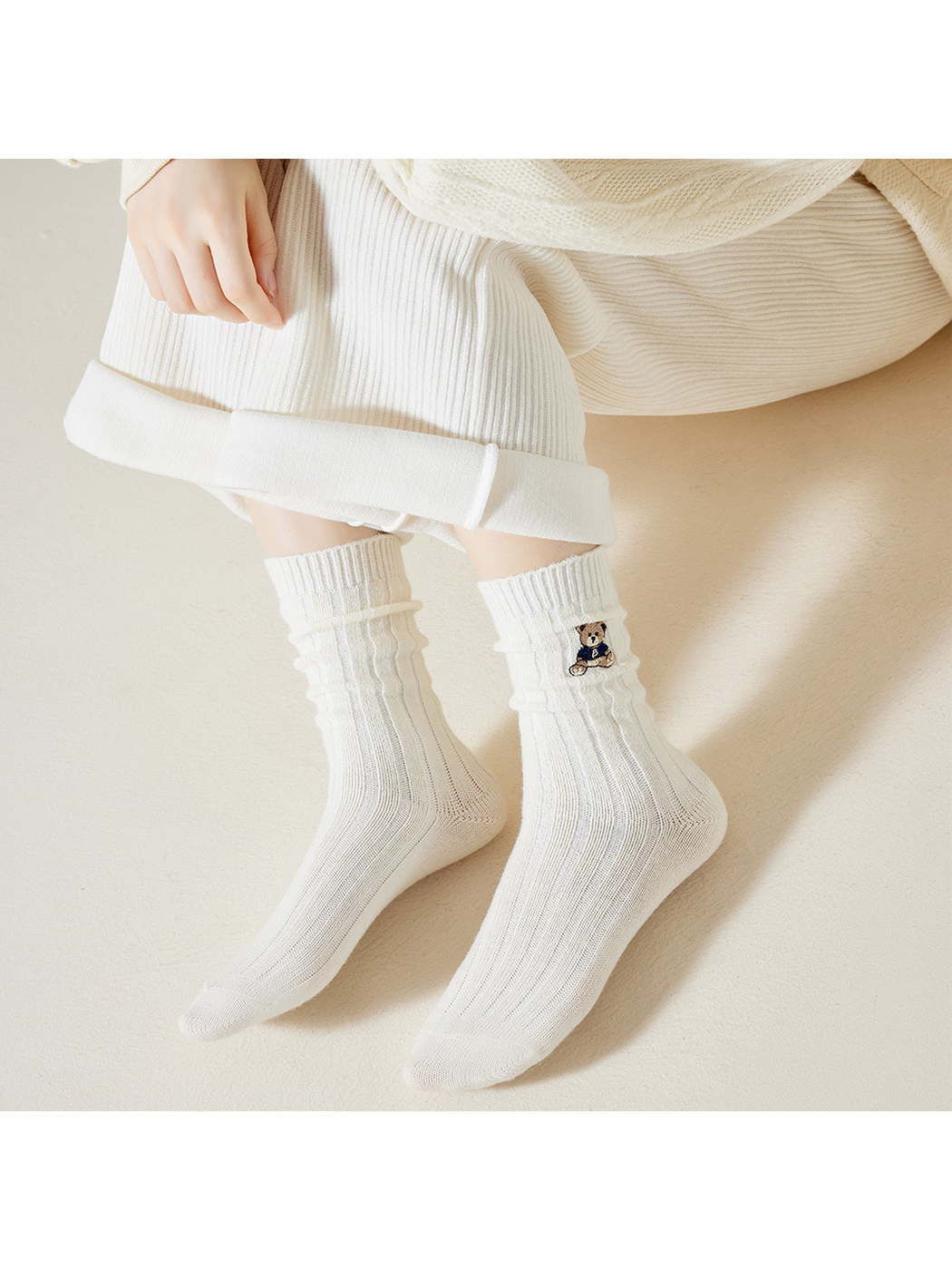 White ribbed crew socks with embroidered teddy bear motif, worn seated