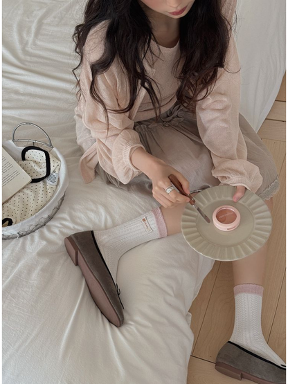 White textured crew socks with pink cuffs and woven label accents worn with gray flats