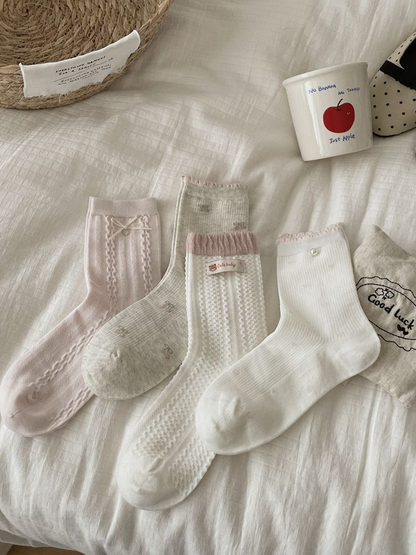 Four pink, gray and white crew sock styles arranged on a cream bedspread