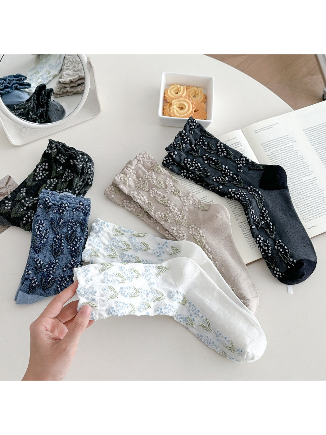 Floral crew socks in five colors with a white pair held in the foreground