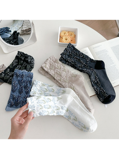 Floral crew socks in five colors with a white pair held in the foreground