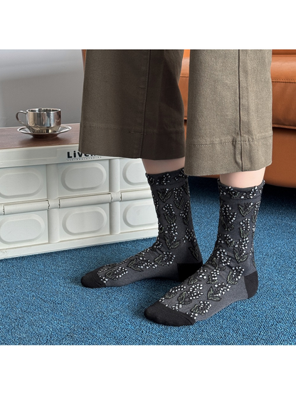 Black floral crew socks worn without shoes against a blue carpet