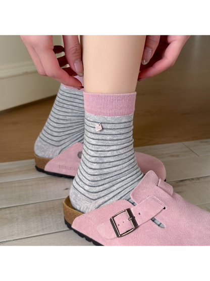 Light gray striped crew socks with pink cuffs styled with pink clogs