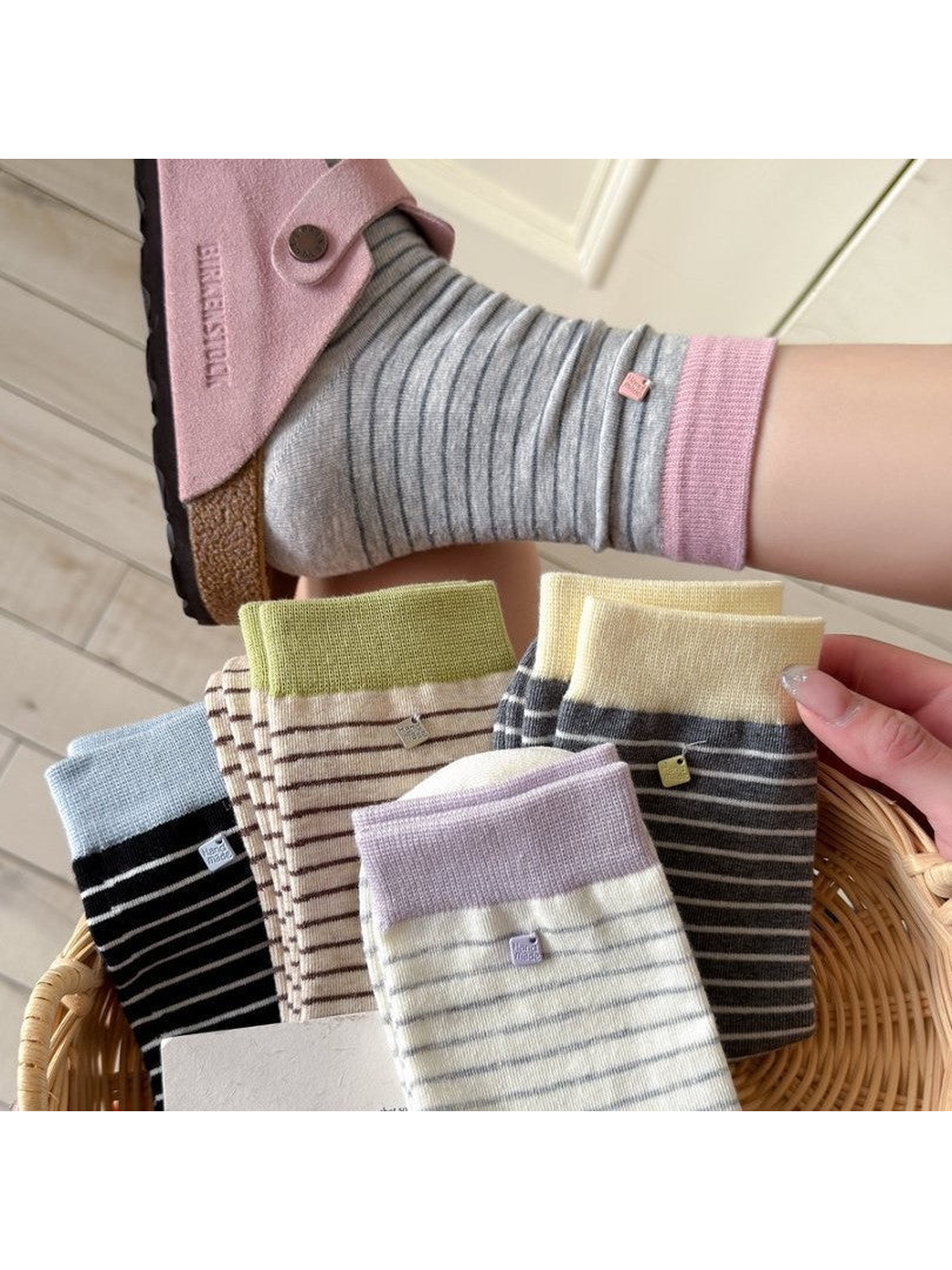 Five striped crew sock colors displayed in a basket with a light gray pair worn above