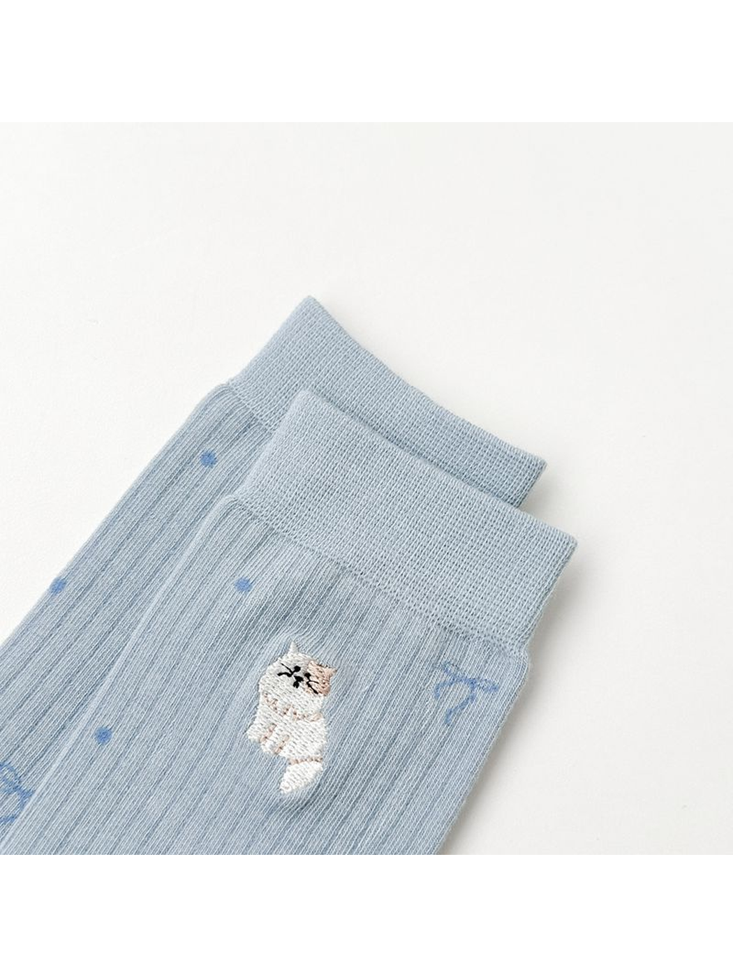 Close-up of an embroidered animal motif below the ribbed cuff of light blue socks
