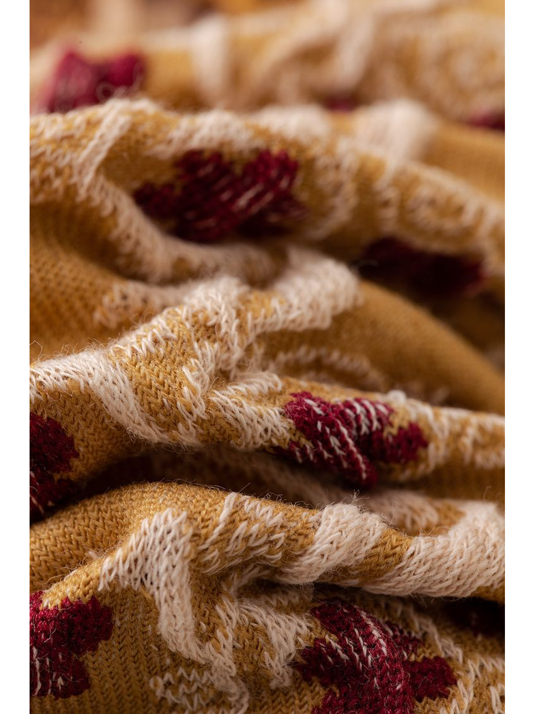 Macro close-up of the raised cream and burgundy motifs on mustard knit