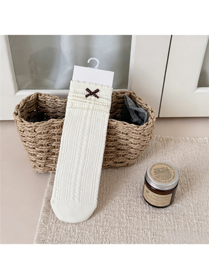 Ivory crew sock with a dark bow, ruffled cuff and vertical textured pattern