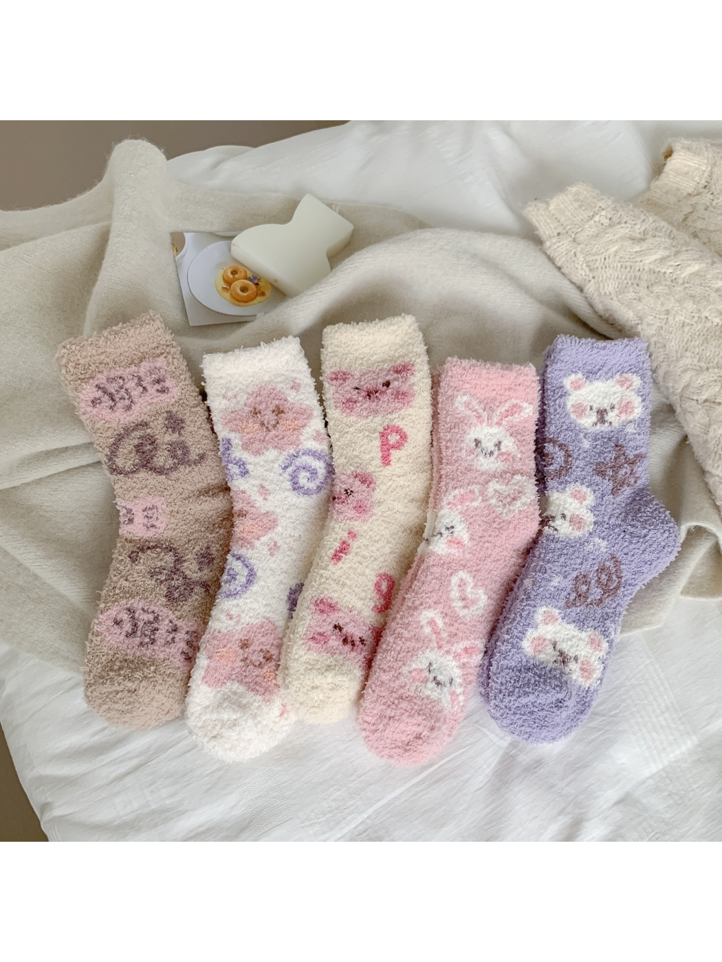 Five fuzzy crew sock designs arranged together in neutral bedding