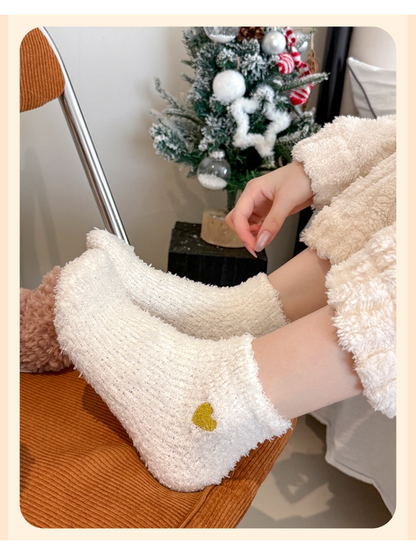 White fuzzy ankle socks with yellow heart embroidery worn in a cozy indoor setting