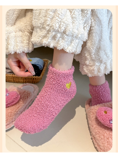 Dusty pink fuzzy ankle socks with yellow heart embroidery shown while stepping from plush slippers
