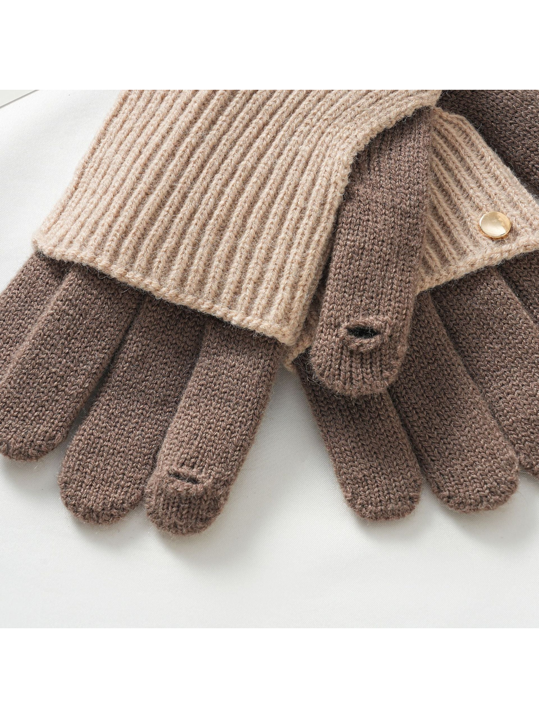 Close-up of fingertip openings and gold-tone button on two-tone knit gloves
