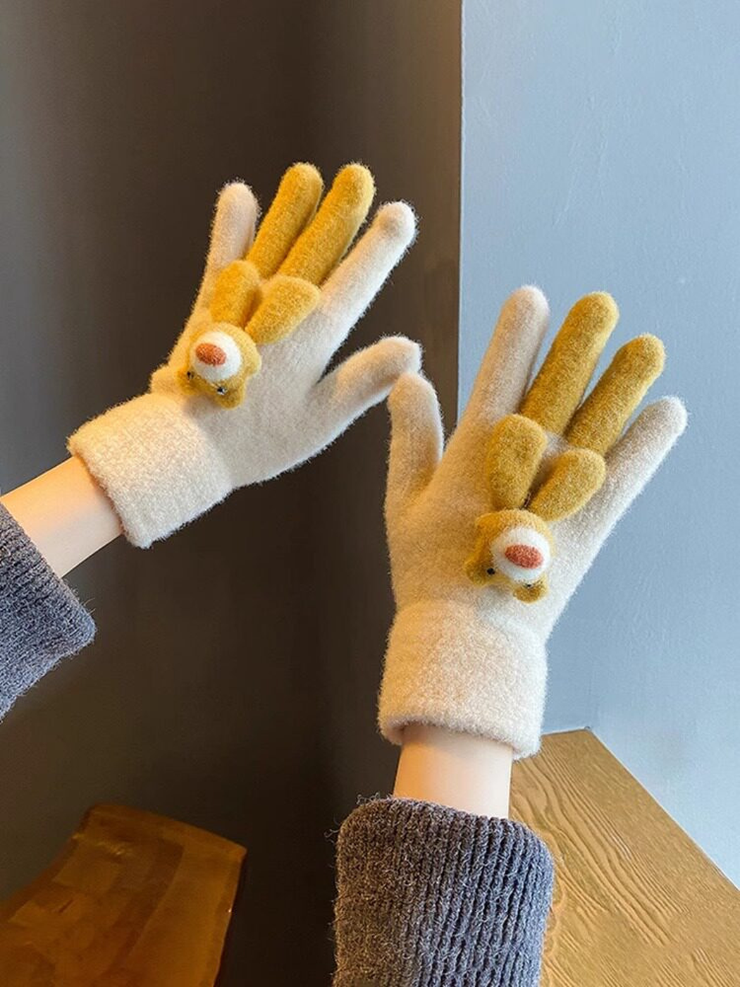 Beige fuzzy gloves with mustard animal appliques in an indoor setting