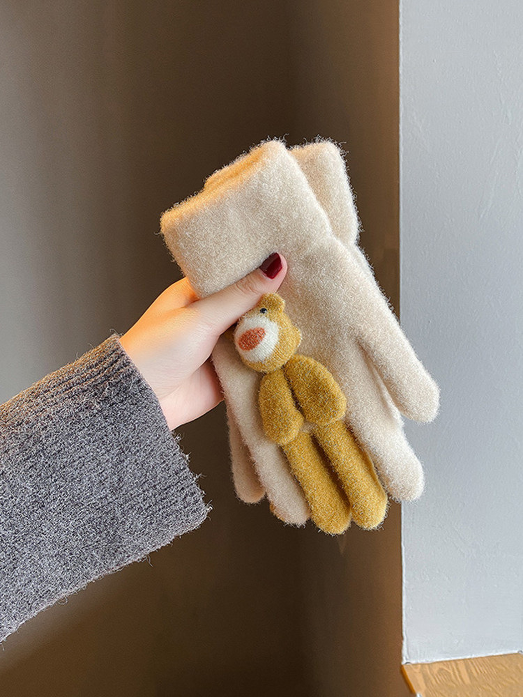 Folded beige gloves with a mustard animal applique held in one hand