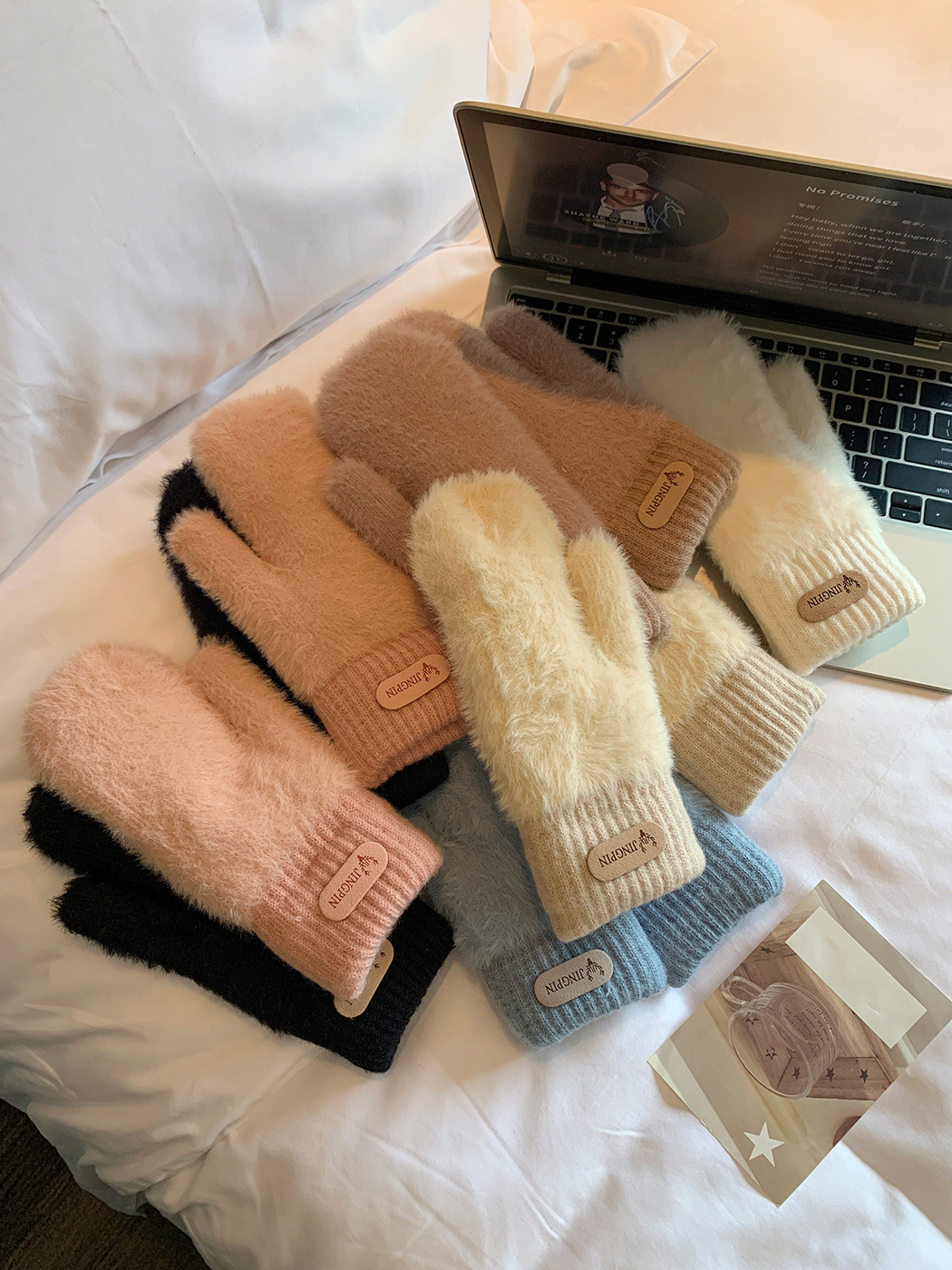 Assorted fuzzy mittens arranged beside a laptop