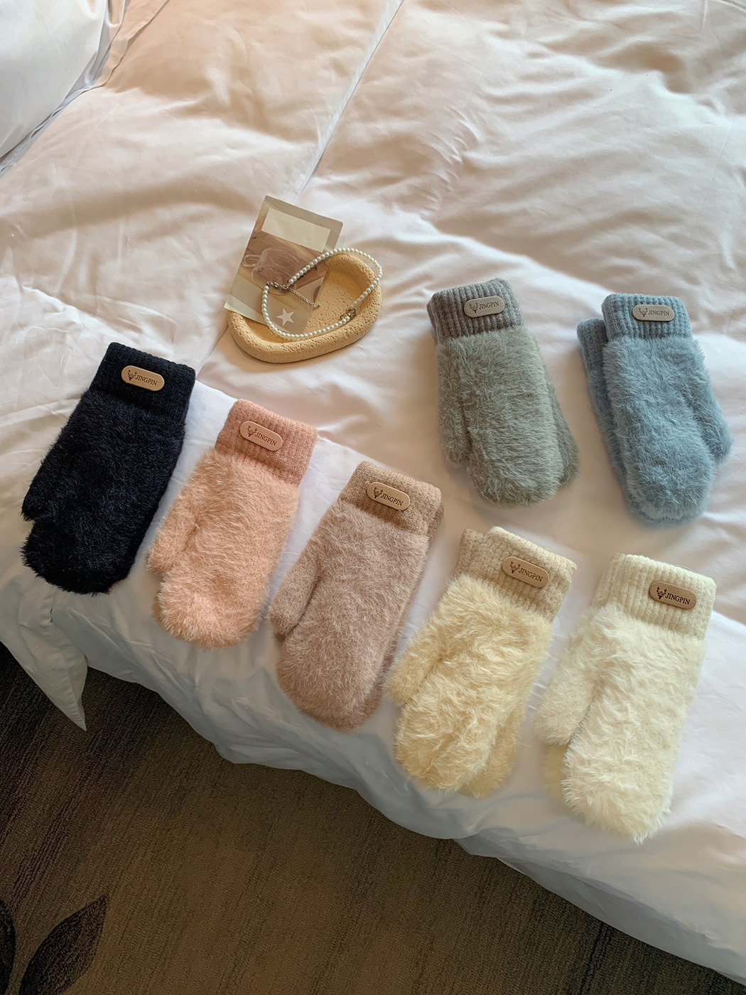 Seven fuzzy mitten color options arranged on a bed