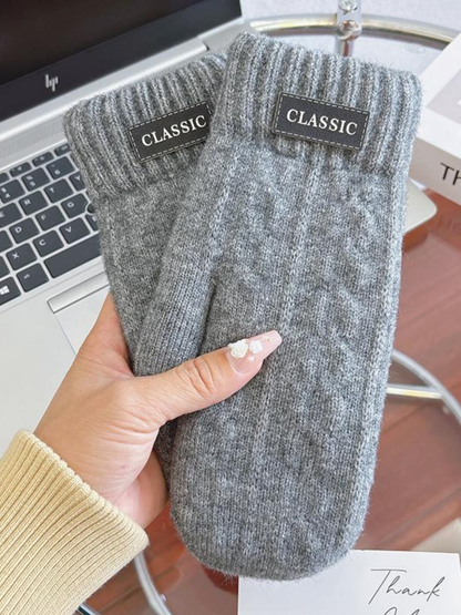 Light gray knit-look mittens with ribbed cuffs and label patches, handheld view