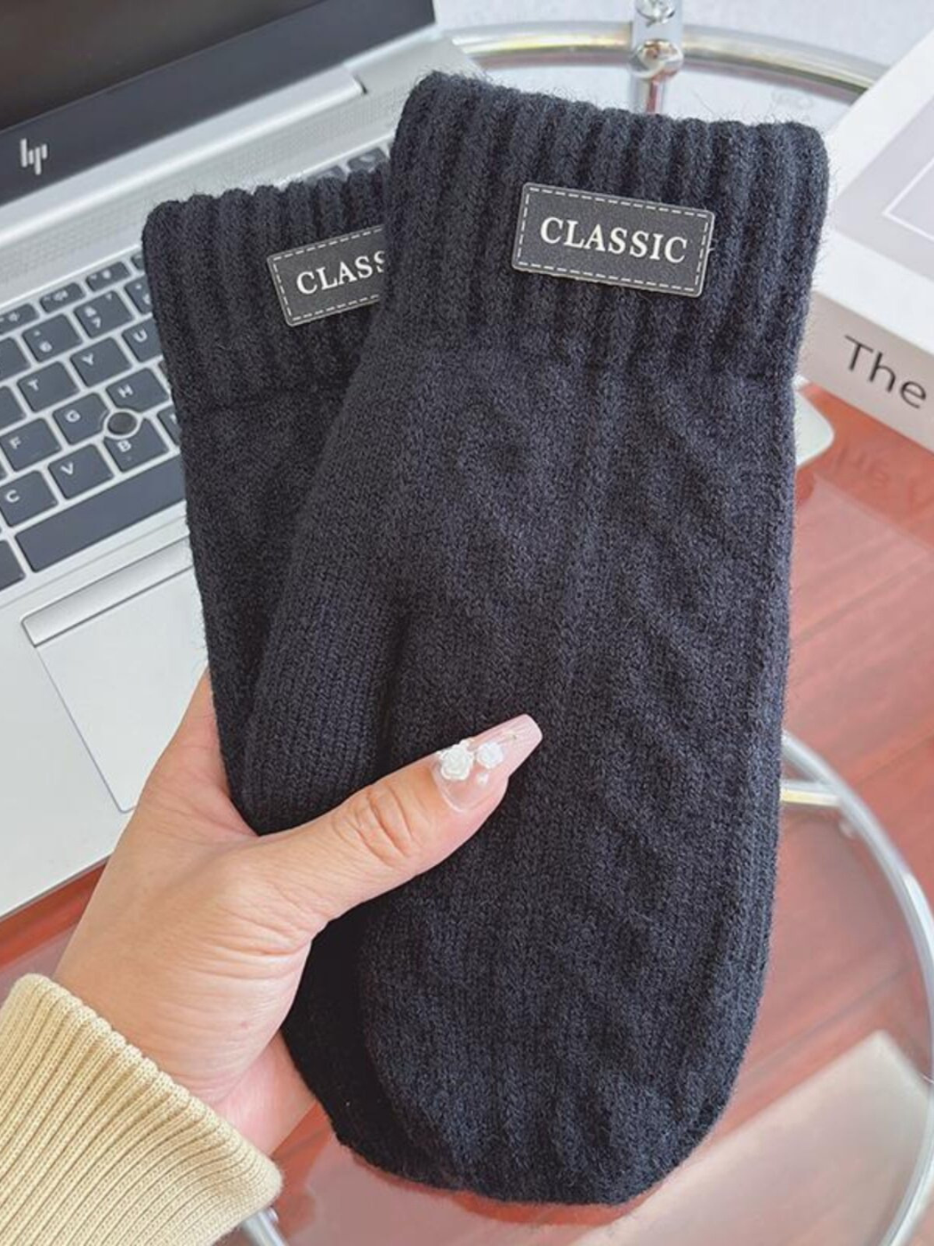 Black knit-look mittens with ribbed cuffs and label patches, handheld view