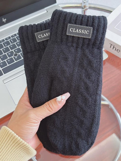 Black knit-look mittens with ribbed cuffs and label patches, handheld view