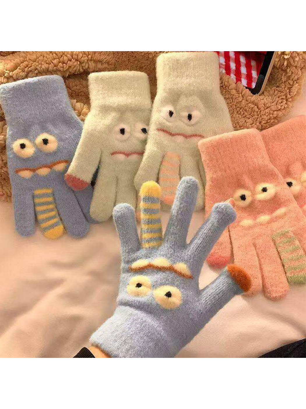 Cartoon face gloves in multiple colors arranged together with a light blue glove worn
