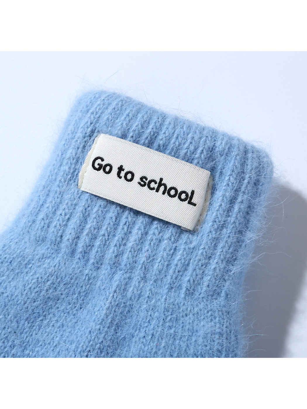 Close-up of a light blue mitten's ribbed cuff and rectangular label