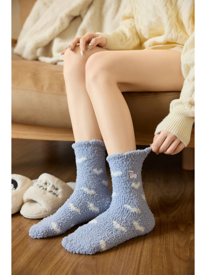 Light blue fuzzy crew socks with white cloud accents and embroidered cats, worn view