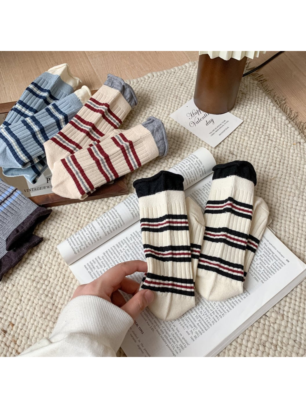 Striped crew socks in multiple colors arranged with an ivory pair in hand