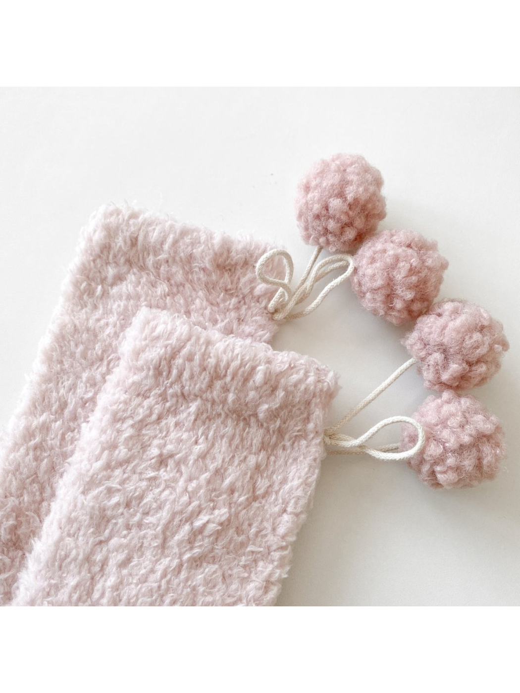Close-up of light pink socks with matching pom-poms and cord ties