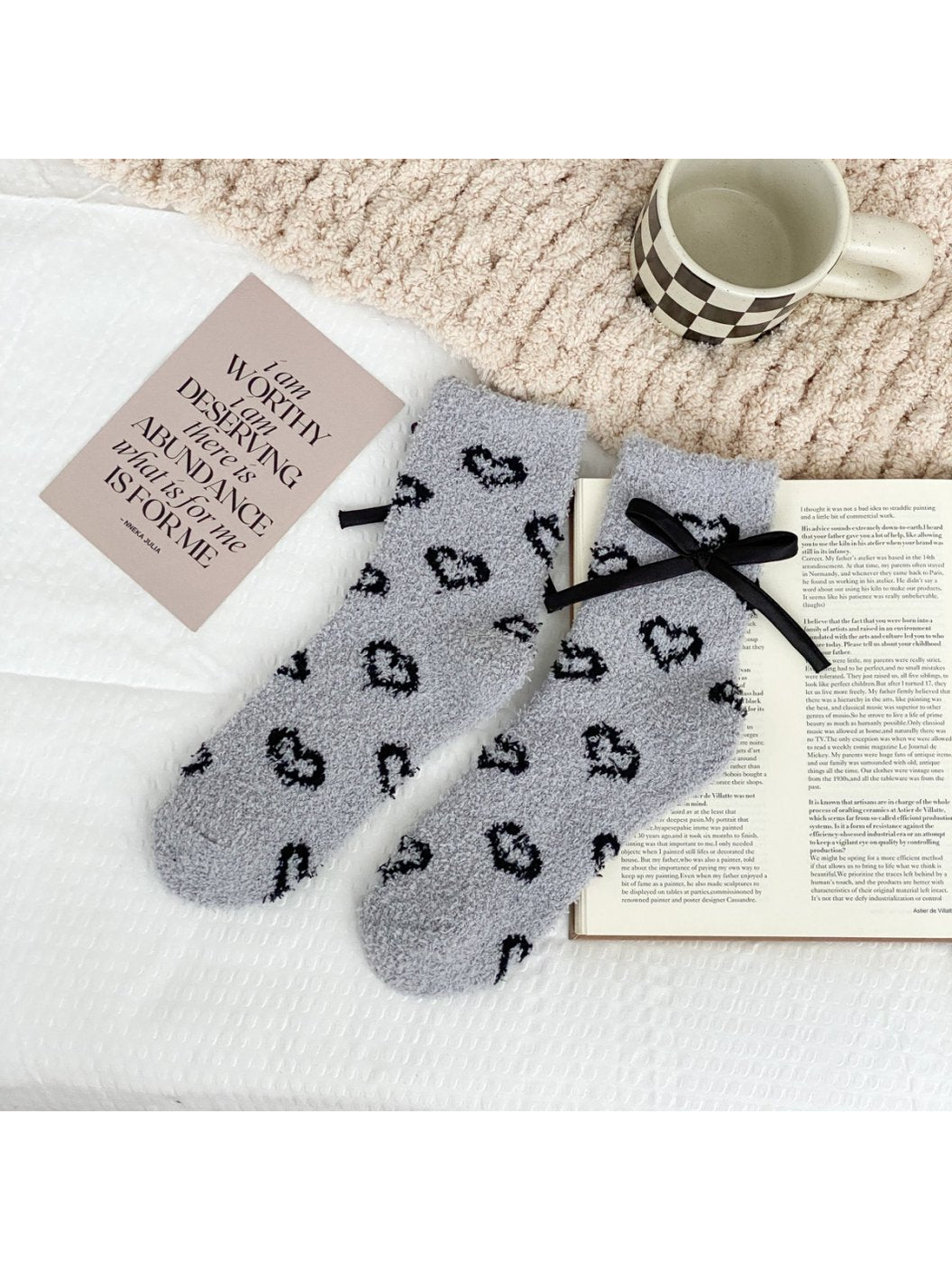 Light gray fuzzy socks with outlined black hearts and a black ribbon bow