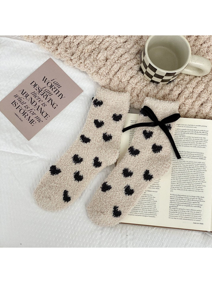 Beige fuzzy socks with small dark hearts and a black ribbon bow