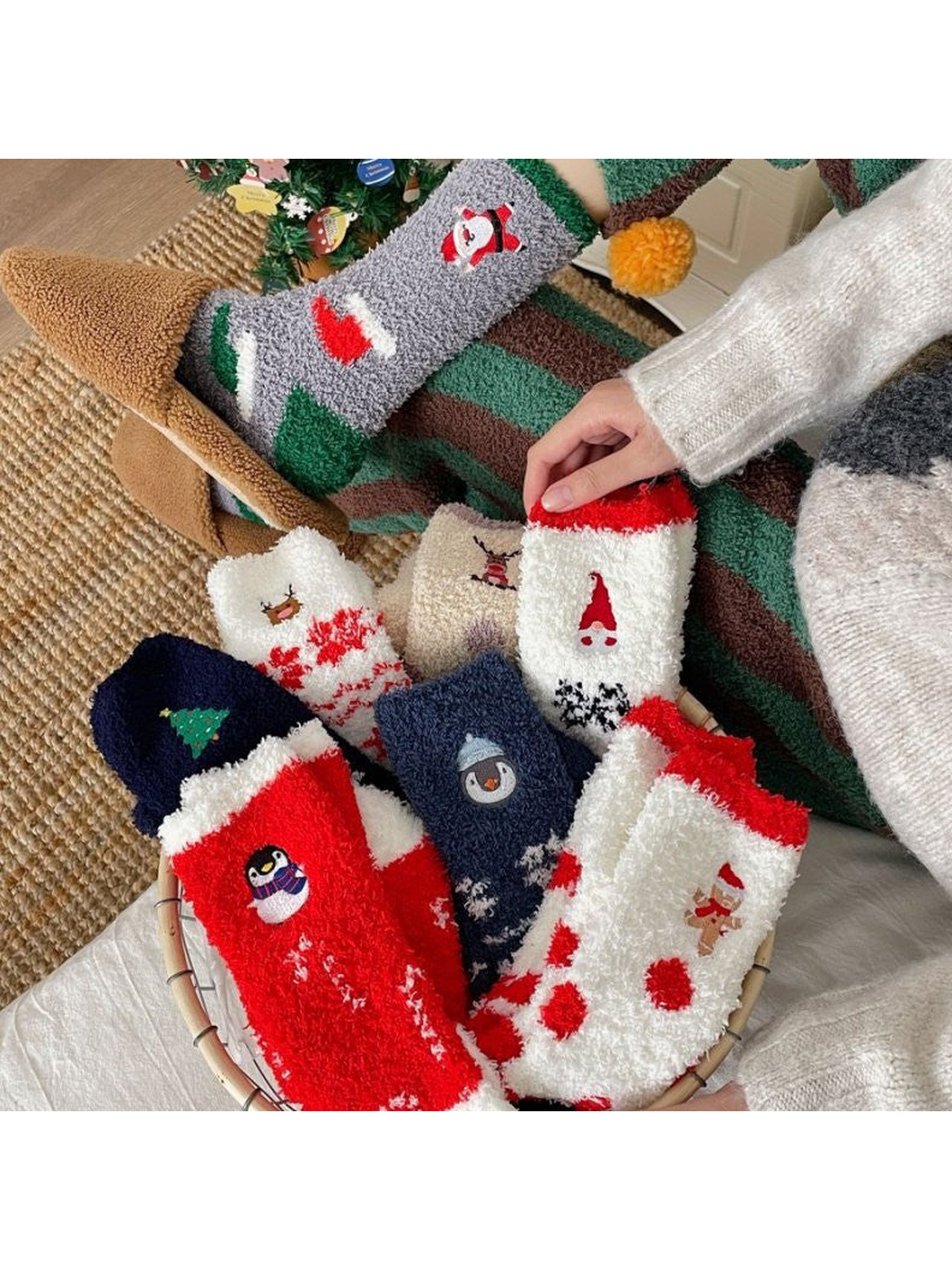 Assorted fuzzy holiday socks arranged in a basket beside a Christmas tree