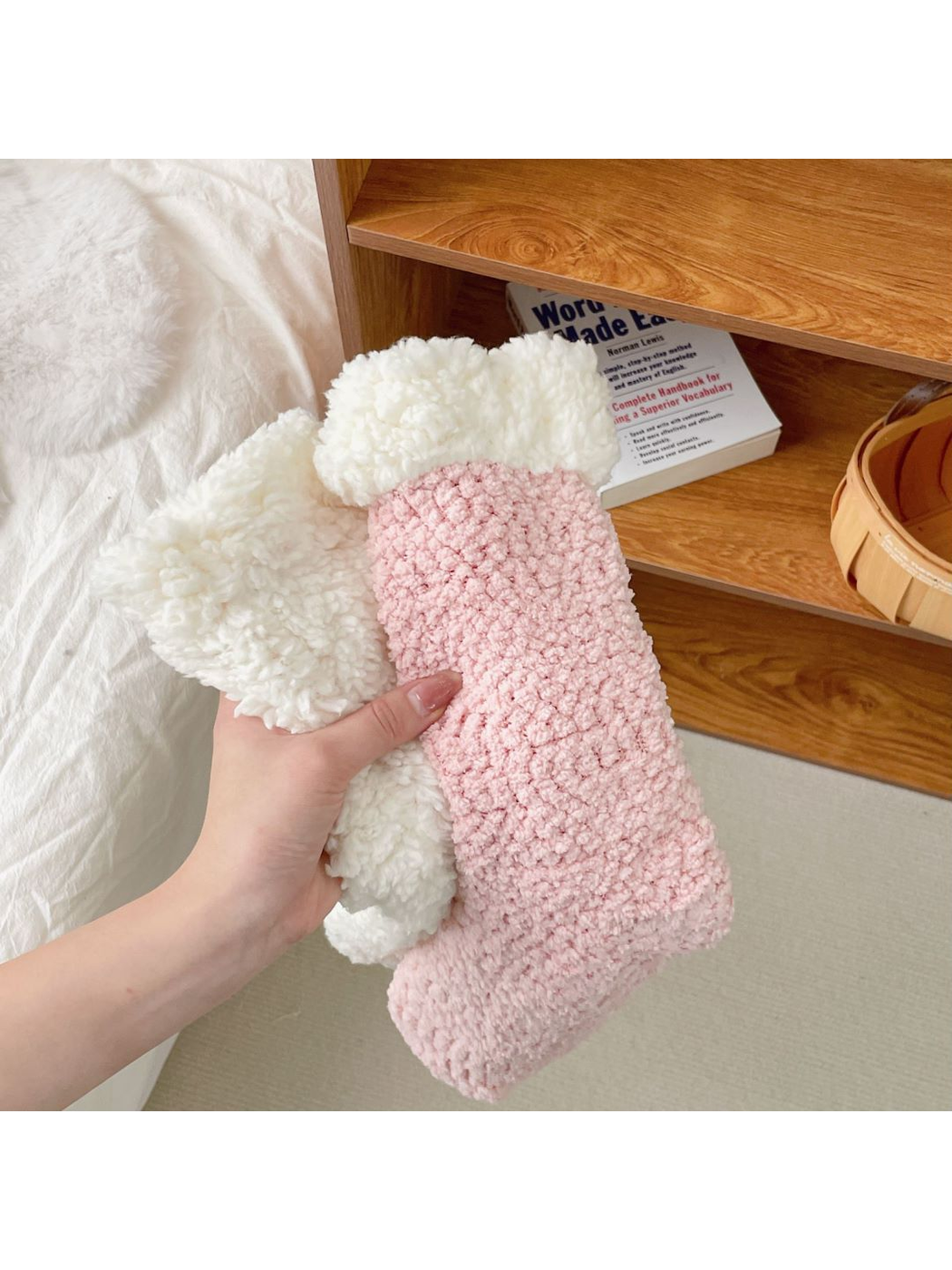 Light pink fuzzy crew socks with ivory cuffs held beside a bed