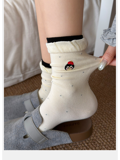 Close-up of an ivory dotted crew sock with character embroidery and ruffled cuff