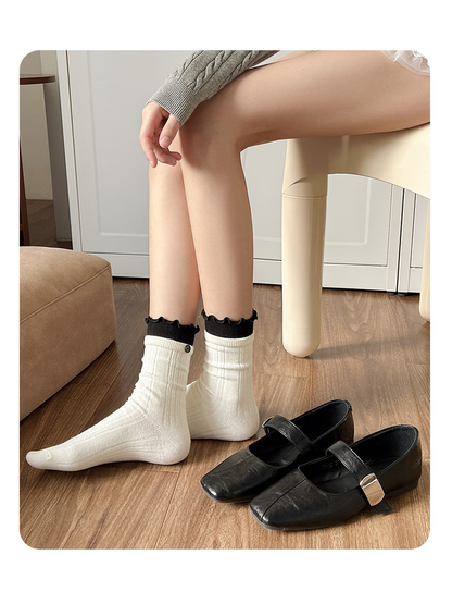White ribbed socks with black ruffle cuffs displayed beside black flats