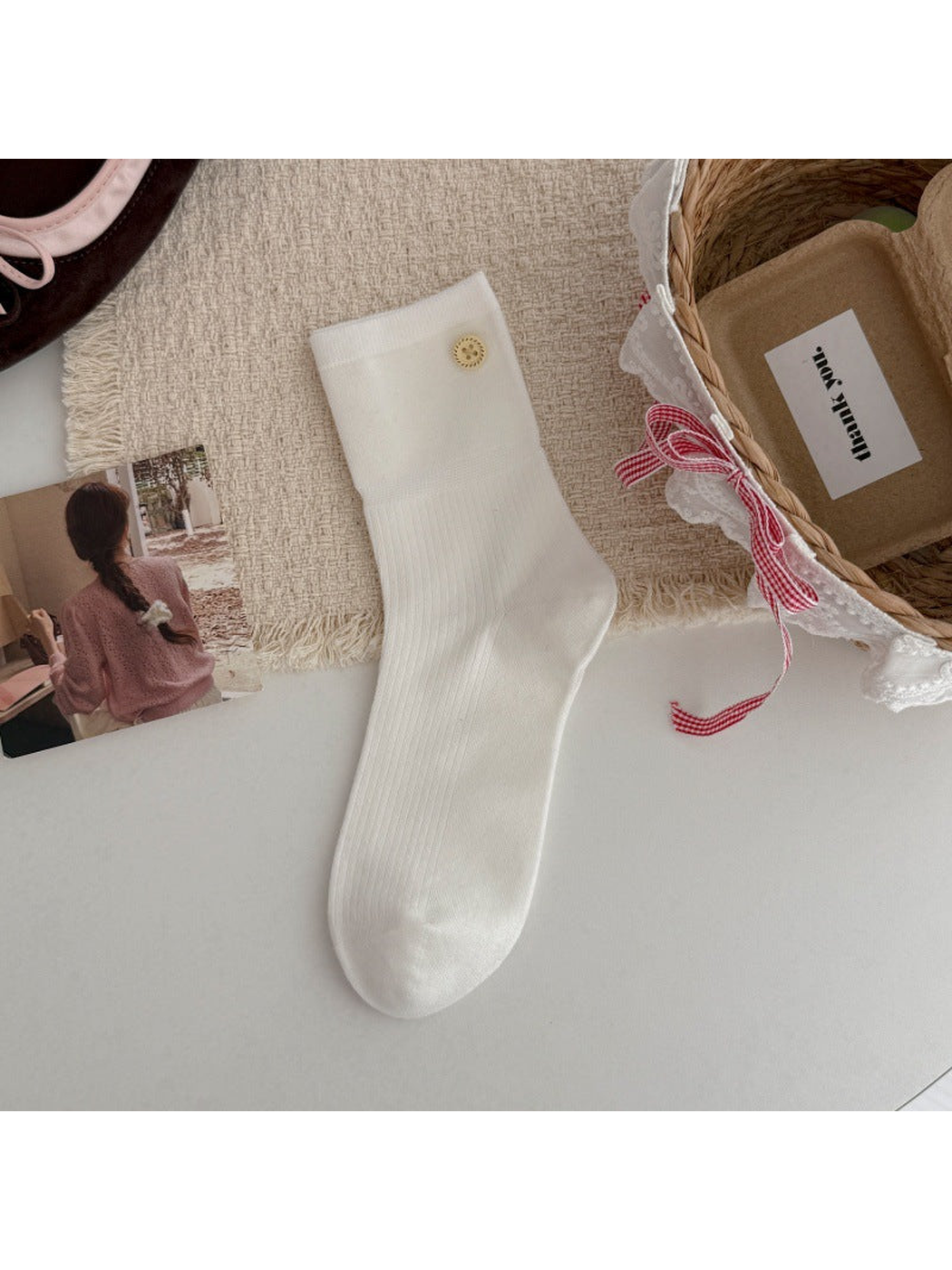 White crew sock with a ribbed leg and gold-tone button accent, flat lay