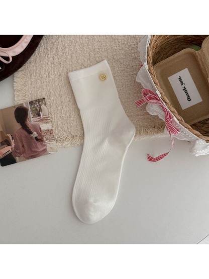 White crew sock with a ribbed leg and gold-tone button accent, flat lay