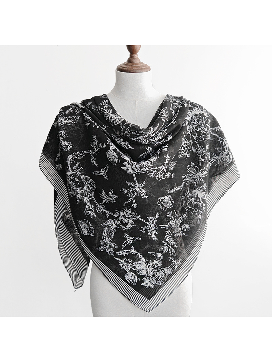 Black patterned scarf styled as a triangular front drape on a dress form